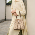 Bild in Galerie-Betrachter laden, Women's beige genuine leather drawstring bucket bag covered in delicate traditional treasure chest pattern Suzhou embroidery, fitted with retro Chinese-style round metal hardware and two-tone leather top handle, model in casual oriental outfit showcasing this versatile daily shoulder bag outdoors