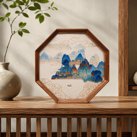 Double-sided embroidery of a blue green mountain landscape with clouds and a boat in an octagonal wooden frame