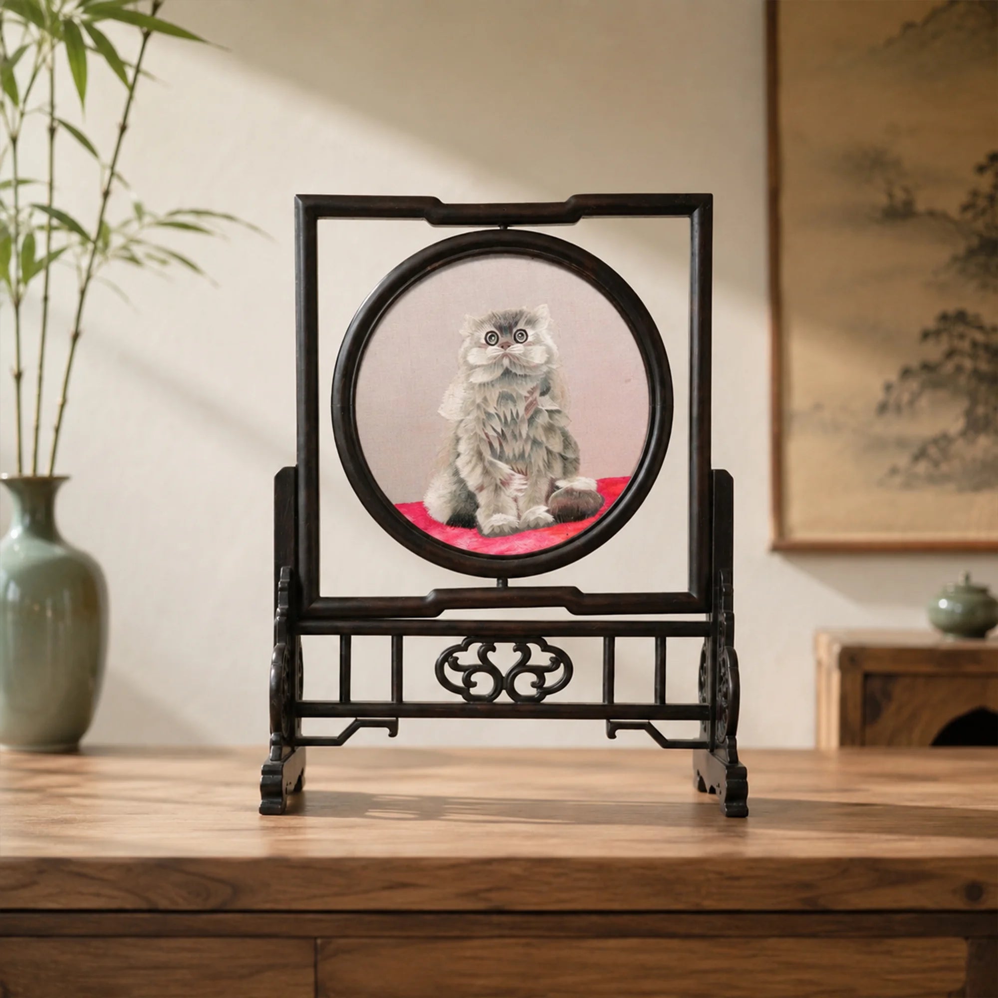 Double-sided embroidery of a fluffy grey cat sitting on a red cushion in a round frame within a rectangular hardwood screen stand with scroll-carved base