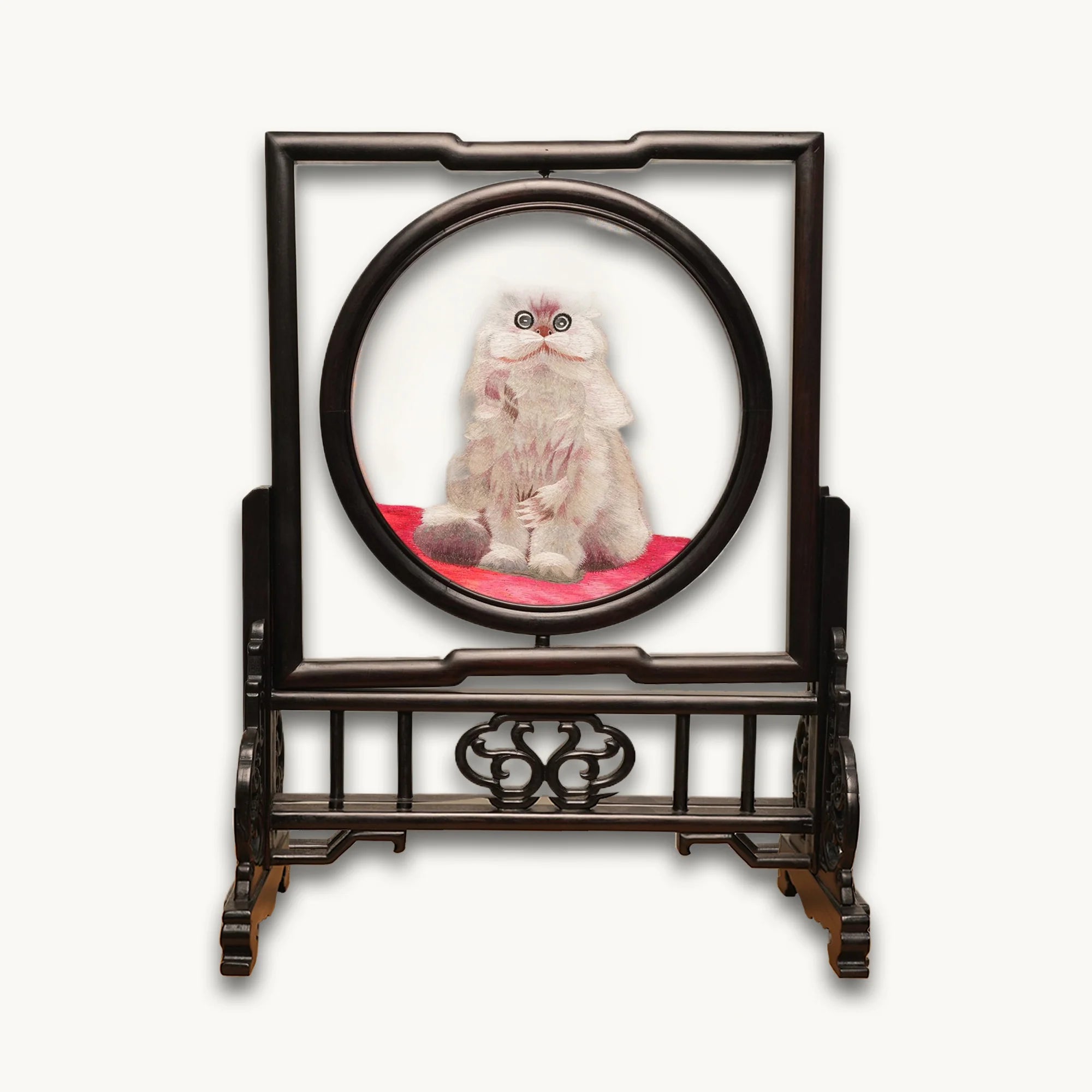 Double-sided embroidery of a fluffy grey cat sitting on a red cushion in a round frame within a rectangular hardwood screen stand with scroll-carved base
