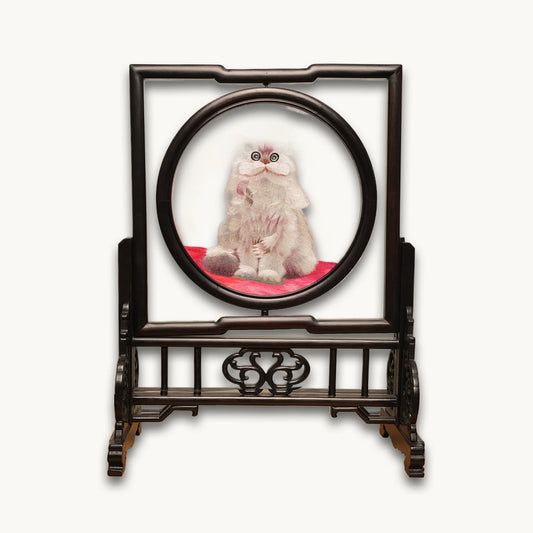 Double-sided embroidery of a fluffy grey cat sitting on a red cushion in a round frame within a rectangular hardwood screen stand with scroll-carved base