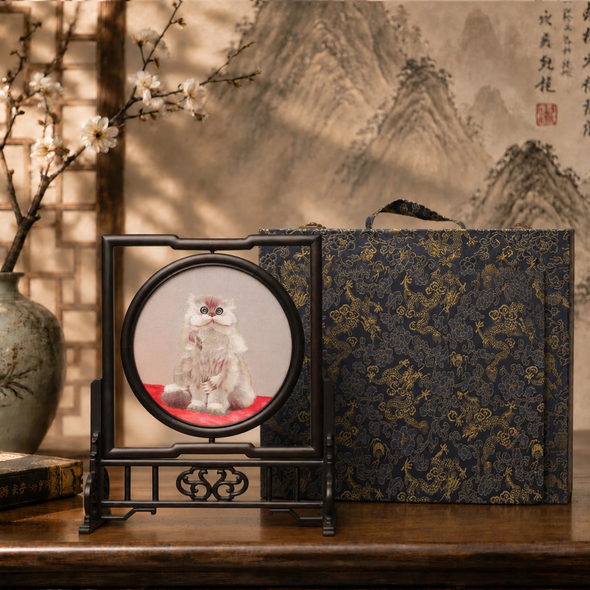 Double-sided embroidery of a fluffy grey cat sitting on a red cushion in a round frame within a rectangular hardwood screen stand with scroll-carved base