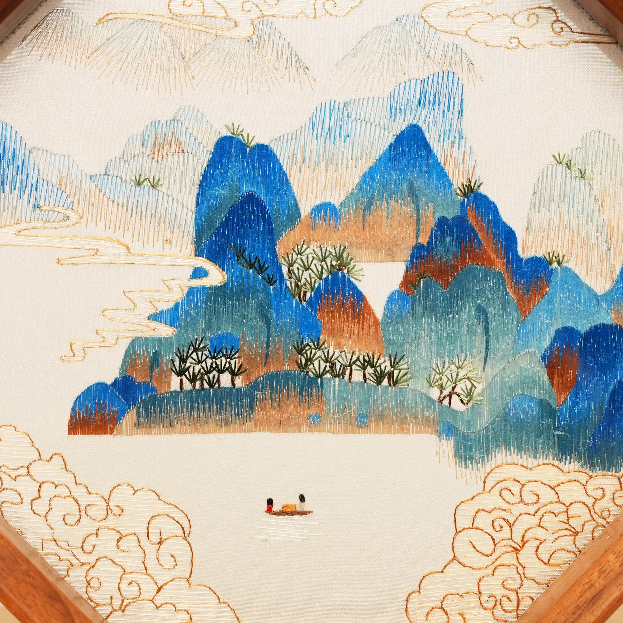Double-sided embroidery of a blue green mountain landscape with clouds and a boat in an octagonal wooden frame