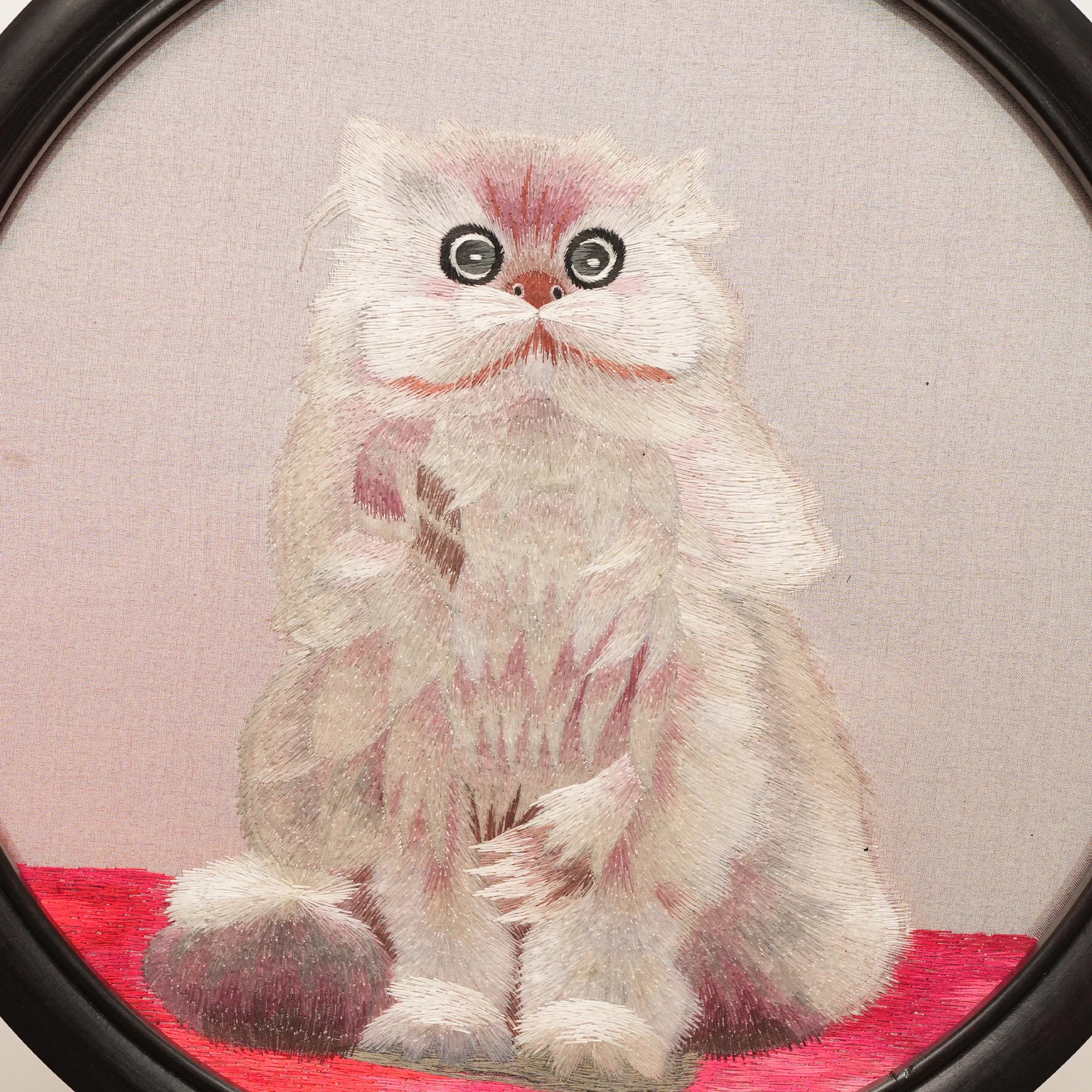 Double-sided embroidery of a fluffy grey cat sitting on a red cushion in a round frame within a rectangular hardwood screen stand with scroll-carved base