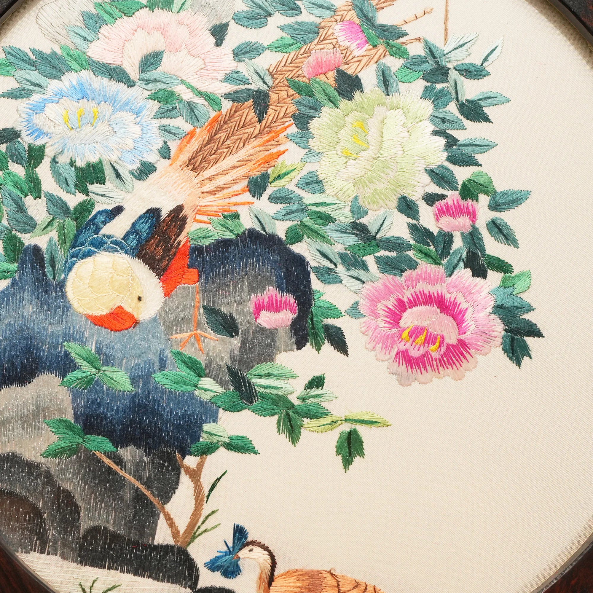 Double-sided embroidery of a golden pheasant on a rock surrounded by colorful peonies in a round dark wood frame on wooden stand