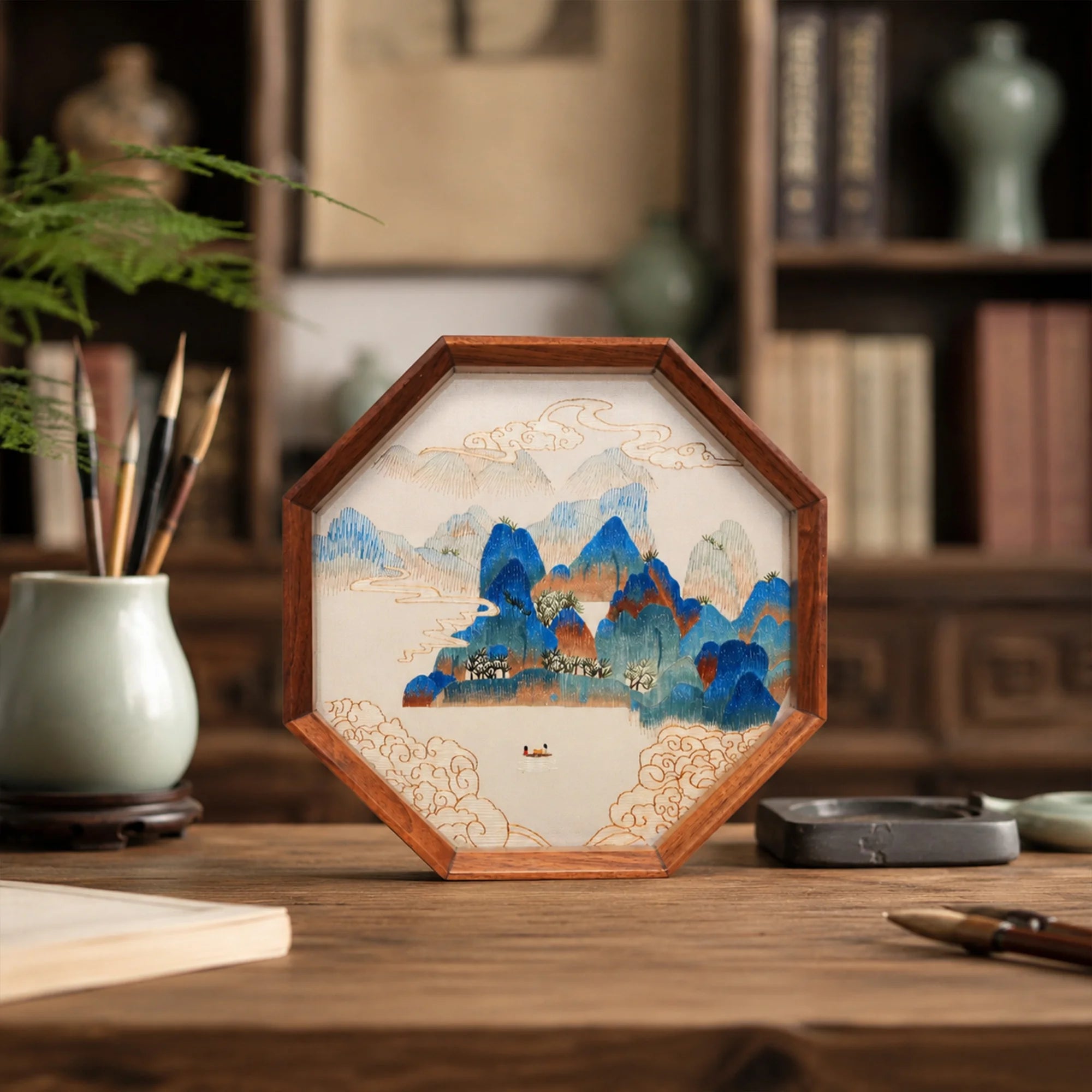 Double-sided embroidery of a blue green mountain landscape with clouds and a boat in an octagonal wooden frame