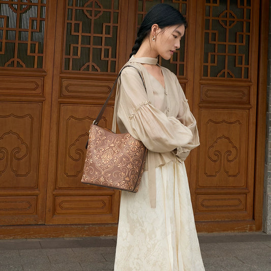 Woman carrying a SinoCrafted brown embroidered tote bag with traditional Chinese scrolling vine patterns in an elegant Chinese-inspired setting.