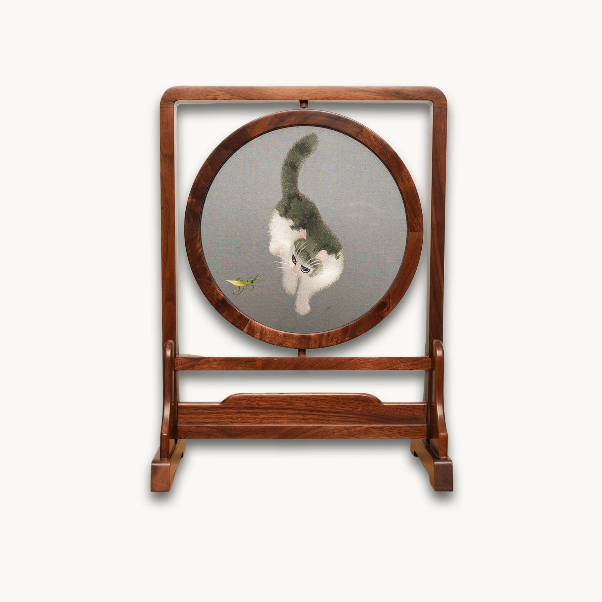 Round double-sided embroidery on hardwood stand showing white and gray cat reaching toward a green grasshopper on gray silk background