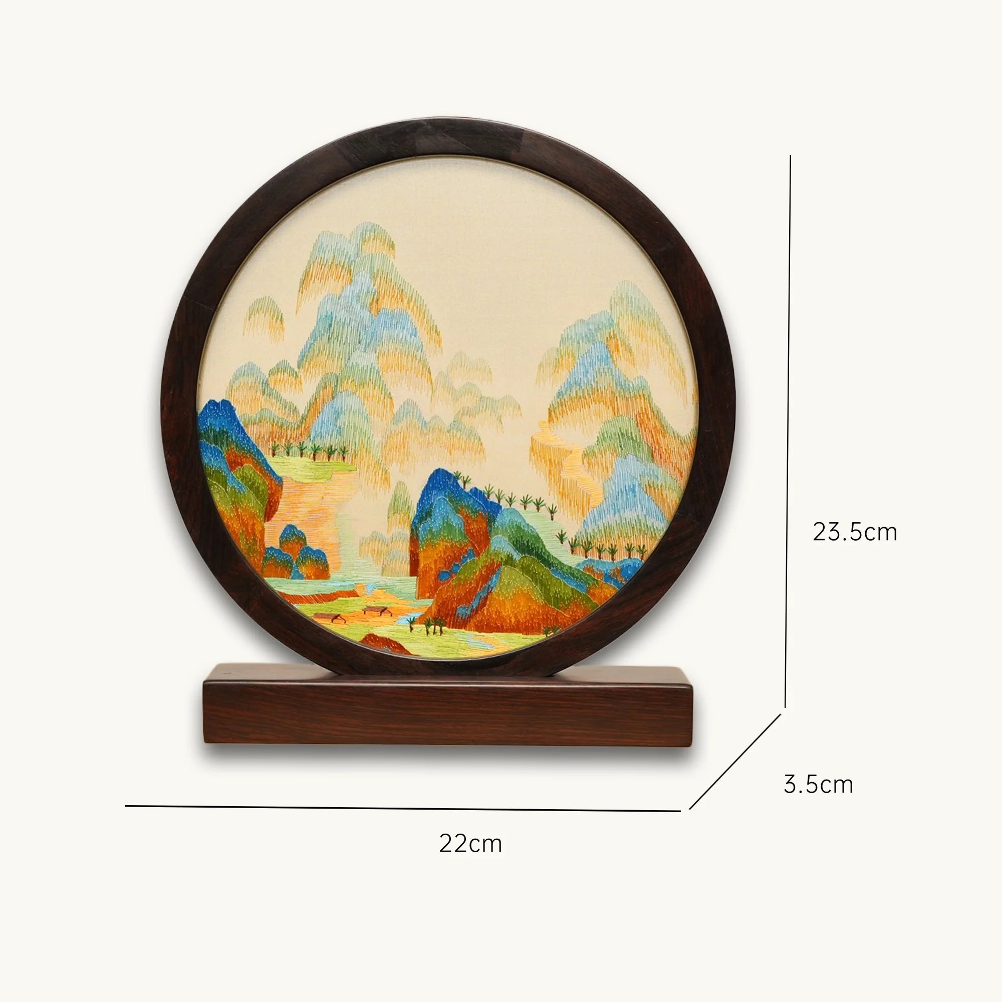 Double-sided embroidery of a colorful blue green mountain landscape in a dark hardwood round frame on wooden stand