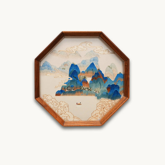 Double-sided embroidery of a blue green mountain landscape with clouds and a boat in an octagonal wooden frame