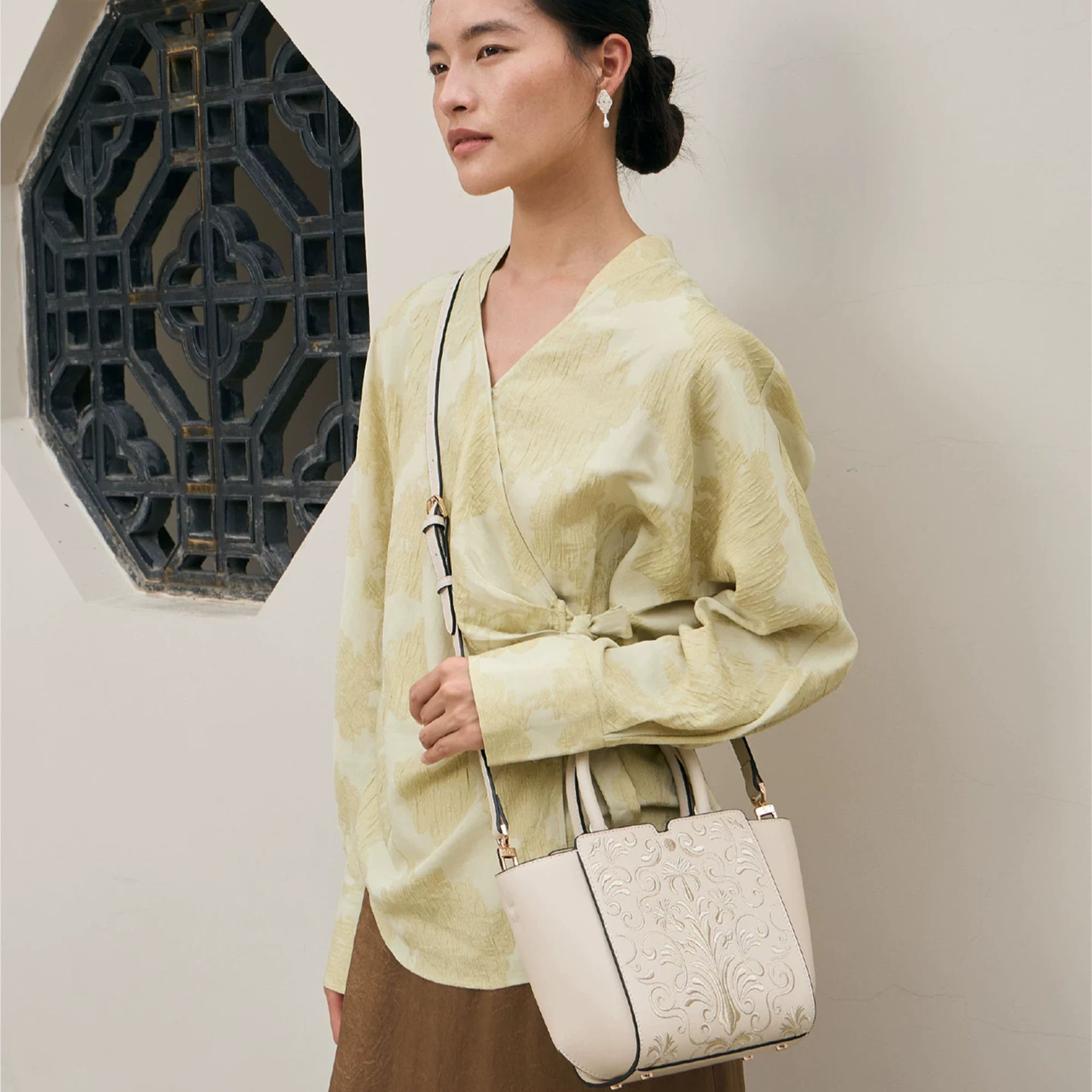 SinoCrafted Suzhou embroidery crossbody handbag with delicate floral patterns, styled by a woman in a modern Chinese-inspired setting.