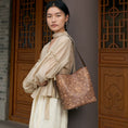 Load image into Gallery viewer, Woman carrying a SinoCrafted brown embroidered tote bag with traditional Chinese scrolling vine patterns in an elegant Chinese-inspired setting.
